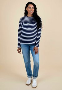 Camisa de manga larga a rayas en azul marino y blanco, combinada con jeans de un azul claro y zapatillas blancas con acentos beige. Tejido suave y corte relajado.