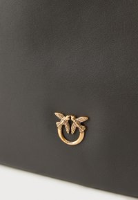 Czarna skórzana torebka z wyrazistym zapięciem w kolorze złotym, które ma kształt dwóch ptaków. Gładka tekstura i minimalistyczny design.
