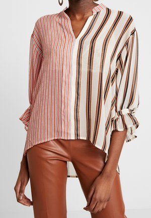 Blusa a righe con scollatura a V, caratterizzata da colori rosso, marrone e crema. Tessuto leggero, maniche lunghe con polsini a volant e orlo asimmetrico.