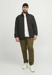 Svart kviltad jacka med grå ärmar, kombinerad med olivgröna cargo-byxor och vita sneakers. En keps fulländar looken.