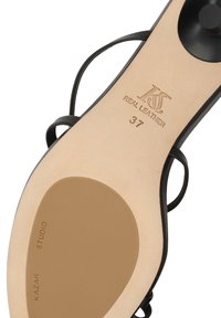 Semelle en cuir de sandale noire à lanières avec la pointure 37, le logo de la marque et Kazar Studio imprimés sur la semelle.