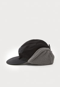 Svart caps med buet skjerm og grå fleece ørelapper. Har sømmer og justerbar stropp bak for en sikker passform.