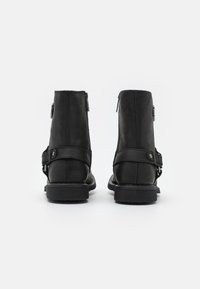 Botas de tobillo de cuero negro con acabado mate, cierre de cremallera y correa decorativa en el lateral. Suela de goma texturizada, diseño robusto.