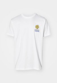 T-shirt de algodão branco com um gráfico colorido de sol e o texto "Em Férias" acima de ondas azuis na área do peito esquerdo. Gola clássica em crew.