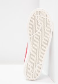 Sneakers med gummisula och en strukturerad vit yttersoffel, med en sidopanel i röd mocka, platt design och zick-zack mönster för grepp.