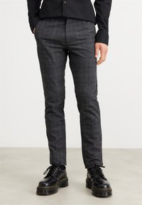 Pantalon à carreaux gris avec une coupe ajustée, confectionné dans un tissu texturé. Associé à des bottes noires à lacets avec une semelle épaisse.