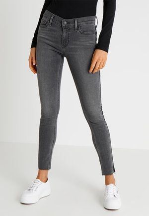 Vaqueros gris ajustados de mezclilla, con cintura de altura media, bolsillos frontales y cremalleras en los tobillos, combinados con zapatillas blancas.