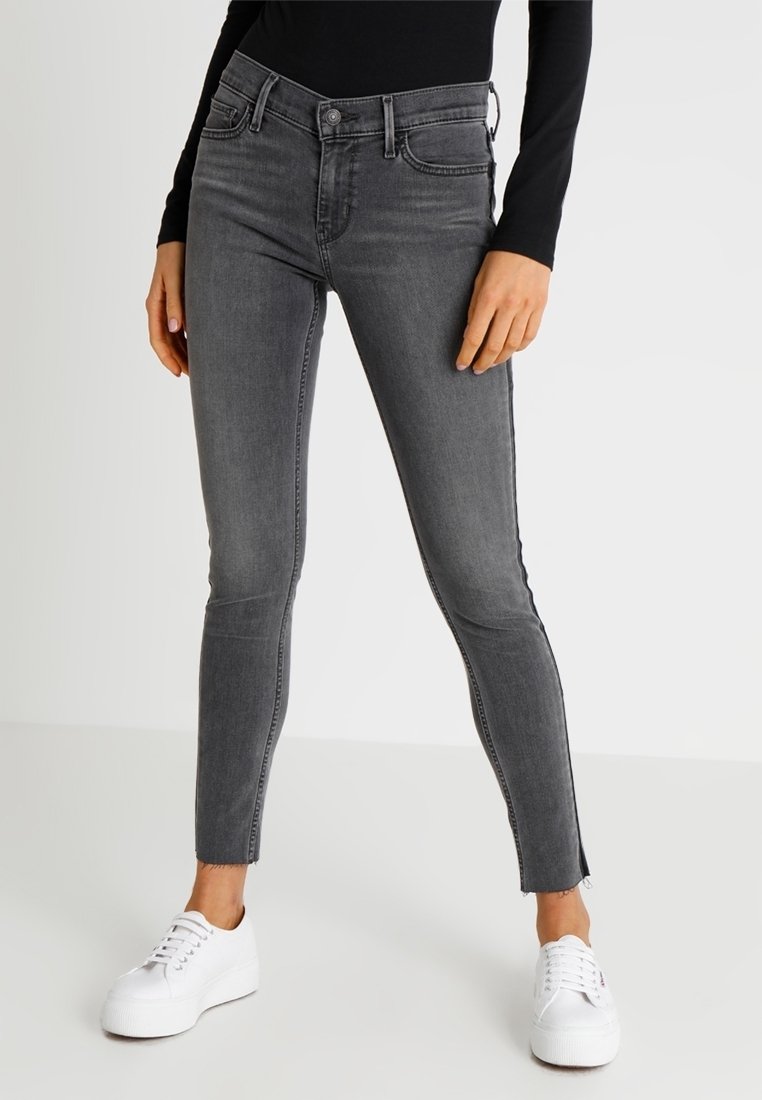 Vaqueros gris ajustados de mezclilla, con cintura de altura media, bolsillos frontales y cremalleras en los tobillos, combinados con zapatillas blancas.