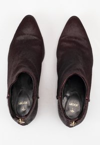 Botas de tobillo burdeos hechas de un material suave y texturizado, con punta afilada y cremallera lateral, que cuentan con un acento de hardware dorado en el interior.