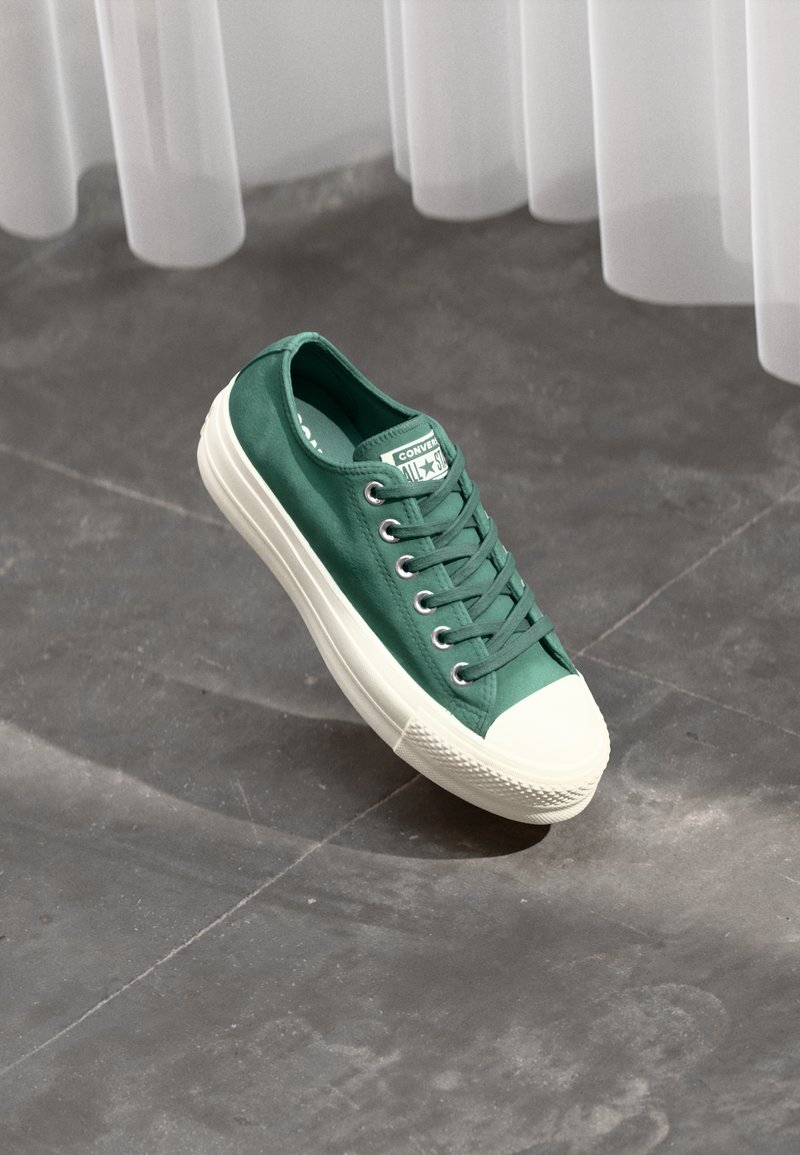 Grønn lerrets-sneaker med hvit gummitå og sidevegg, med seks hull og en klassisk snøring.