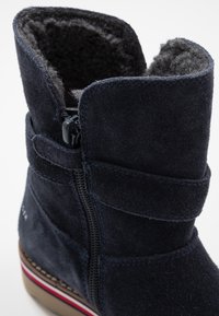 Granatowe zamszowe botki za kostkę z bocznym zamkiem błyskawicznym, miękką podszewką wewnętrzną oraz kontrastową białą i czerwoną paskowaną podeszwą. Posiadają rzep.