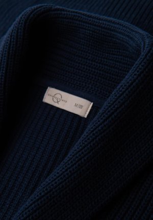 Námořnická modrá pletená cardigan se žebrovanou strukturou. Má široký límec a štítek přišitý uvnitř. Hladká látka s lehkým pocitem.