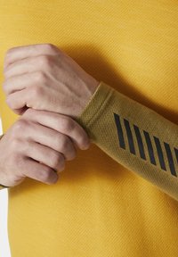 Žlutá texturovaná košile s dlouhým rukávem a hnědou akcentovanou rukávovou částí, která má černé diagonální pruhy. Rukáv se dobře obepíná kolem zápěstí.