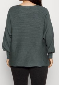 Pull côtelé vert foncé avec un large décolleté et des manches chauve-souris, présentant un tissu texturé et une coupe décontractée.