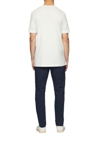 Witte katoenen t-shirt met een ronde hals, gecombineerd met marineblauwe katoenen broek. De outfit heeft een minimalistisch design met een relaxte pasvorm.