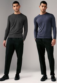 Zwei Models stehen nebeneinander, tragen langärmelige, figuroptimierte Pullover in Dunkelgrau und Marineblau, kombiniert mit maßgeschneiderten schwarzen Hosen und schwarzen Schuhen.