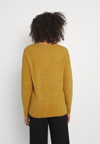 Musztardowy żółty sweter dzianinowy o luźnym kroju, prążkowanej fakturze i opadających ramionach. Długie rękawy i okrągły dekolt.