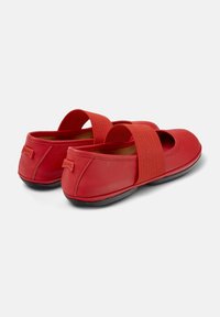 Zapatos de cuero rojo con puntera redondeada, tira elástica sobre el empeine y suela de goma negra. Con textura suave y diseño sencillo.