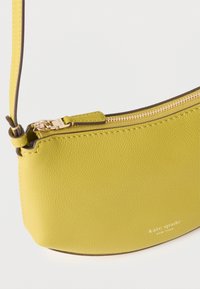 Κίτρινη δερμάτινη τσάντα ώμου με χρυσό φερμουάρ και ρυθμιζόμενο λουράκι, με μικρό λευκό λογότυπο "kate spade new york" στο μπροστινό μέρος.