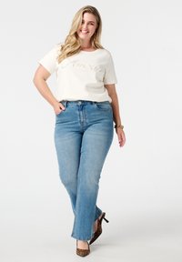 T-shirt crème à manches courtes avec texte perlé, associé à un jean flare bleu clair et des escarpins à imprimé léopard.