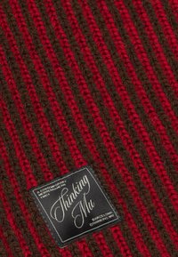 Red and brown striped knitted fabric with a black label reading "Thinking Mu" and "Barcelona" in white script.