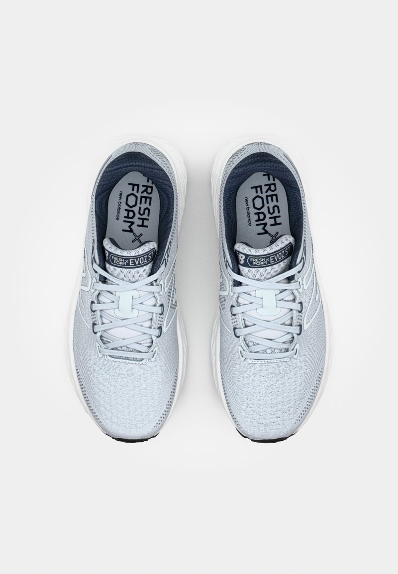 Zapatillas de running de color gris claro con parte superior de malla texturizada, suela de amortiguación blanca y detalles reflectantes en los cordones y el logo.