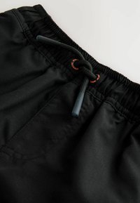 Costumi da bagno neri con vita elastica, dotati di un laccio nero e un piccolo dettaglio del logo arancione a contrasto. Tessuto dalla consistenza morbida.