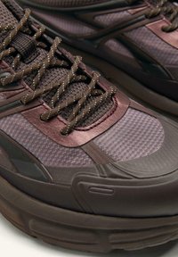 Nærbillede af mørkebrune og malvesfarvede sportssko med tekstureret stof, mønstrede snørebånd og tykke gummi-såler.