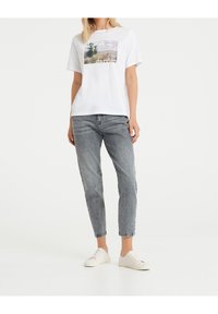 Bílý krátký rukáv T-shirt s předním potiskem krajiny a textem. Šedé džínové kalhoty se zúženou nohavicí a bílé tenisky. Jednoduchý design.