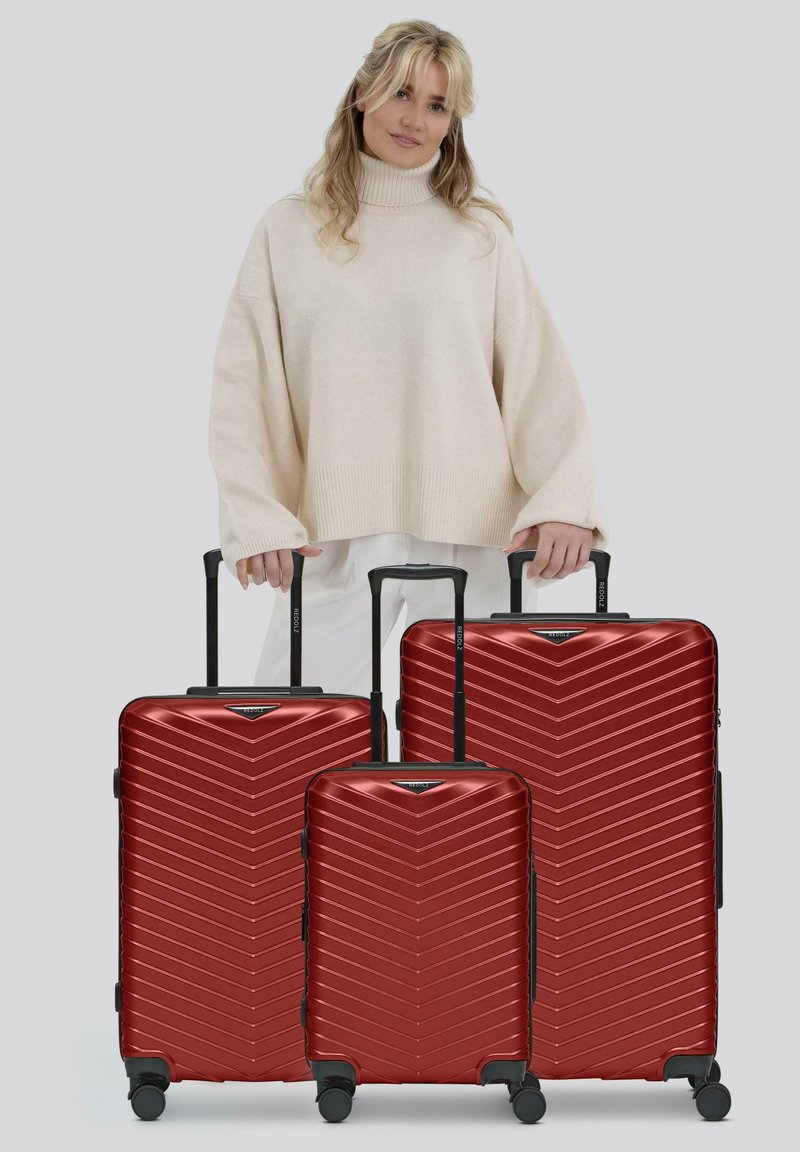 Drei rote Hartschalenkoffer mit einem Chevron-Muster in verschiedenen Größen, schwarzen Griffen und Rädern. Vor einem neutralen Hintergrund.