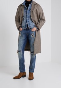 Brun hounds-tooth kappa över blå denimjacka, slitna blå jeans med knäskärningar och bruna mocka ankelboots.