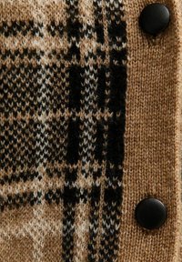 Cardigan en tricot présentant un motif à carreaux brun et noir, fil texturé et détail de bouton noir sur le côté droit.