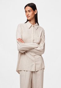 Camicia beige con bottoni, a righe verticali, maniche lunghe e taschino sul petto. Rifinita con colletto a punta e vestibilità rilassata.