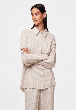 Chemise beige à boutons avec des rayures verticales, à manches longues et une poche poitrine. Fini avec un col pointu et une coupe décontractée.