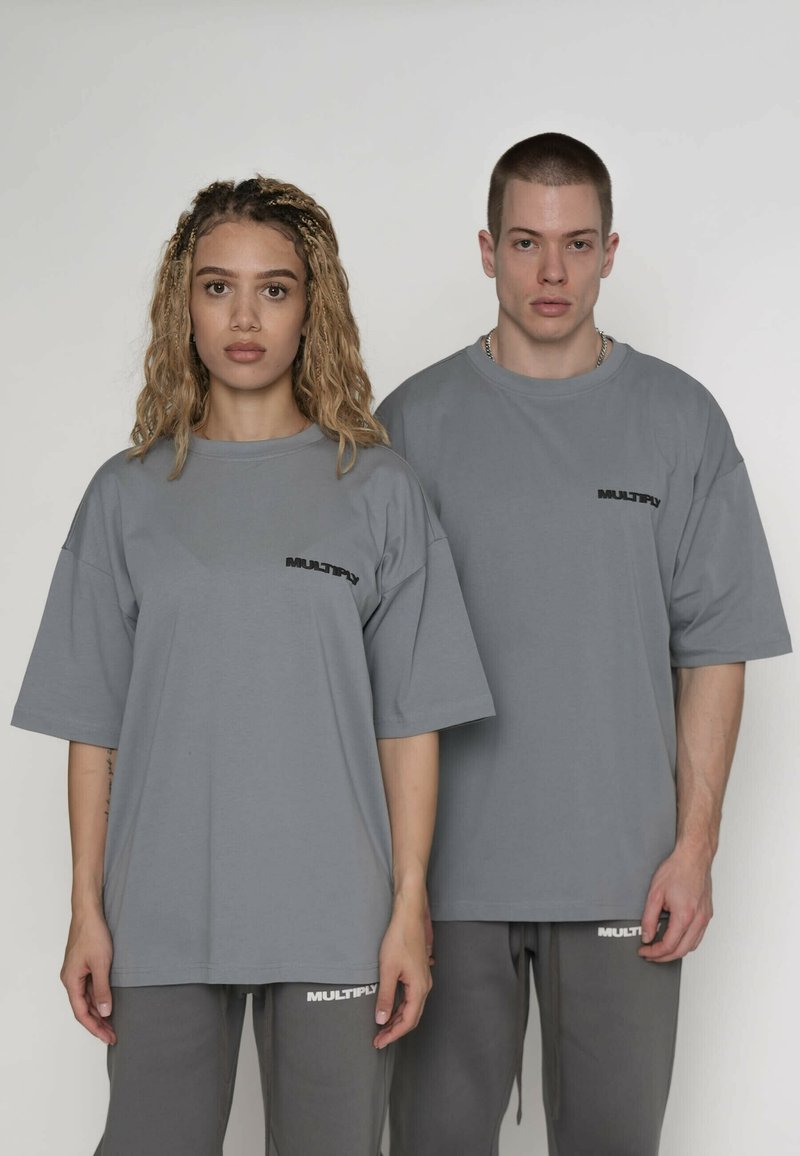 Grå oversized t-shirts med korte ærmer, som har en lille "MULTIPLY"-logo i sort på brystet. Bæres sammen med matchende grå joggingbukser.