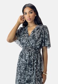 Schwarzes Blumenkleid mit kurzen, puffierten Ärmeln; gesmokte Taille; mit weißen Blumenmustern und einem tiefen V-Ausschnitt.