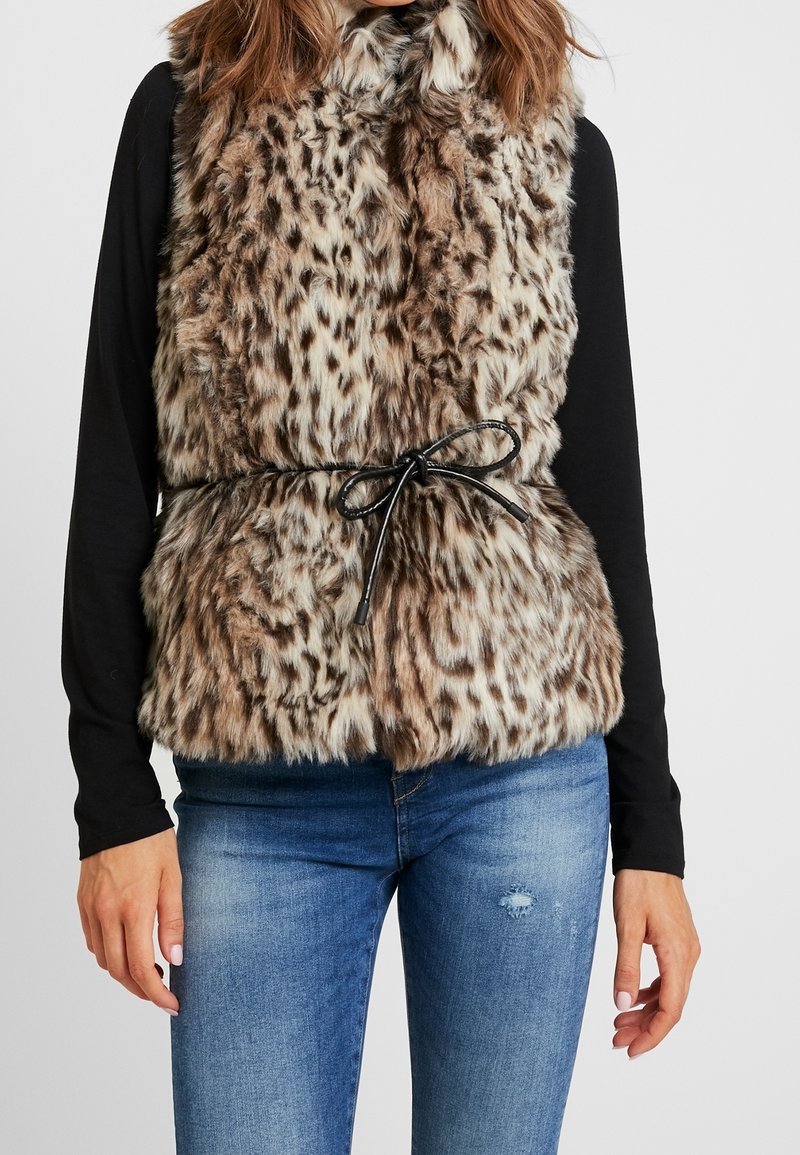 Faux-Fur-Weste mit einem Leopardenmuster in Braun und Creme, ausgestattet mit einem Kragen und einem schwarzen Kordelzuggürtel. Trägt man über einem schwarzen Langarmoberteil.