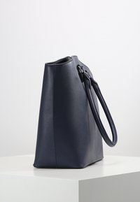 Námořnická kožená taška s pevným tvarem, hladkým povrchem a jedním uchopením. Vyznačuje se minimalistickým designem a plochým dnem.