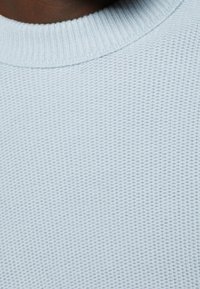 Hellblau strukturierter Pullover mit geripptem Kragen und feinem Netzmuster auf dem Stoff. Fokus auf Wärme und Atmungsaktivität.