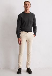 Lichtbeige corduroy broek en een donkergrijze gebreide trui worden gedragen met zwarte veterschoenen. De outfit heeft getailleerde silhouetten en zachte texturen.