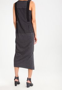 Grå ärmlös klänning med svart randmönster, figursydd midja och en lång, flödande kjol; matchad med svarta klackskor med ankelsnörning.