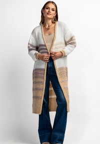 Sweter na drutach w kolorze białym z beżowymi i lawendowymi paskami. Otwarty przód, długie rękawy i luźny krój, zestawiony z niebieskimi dzwonami.