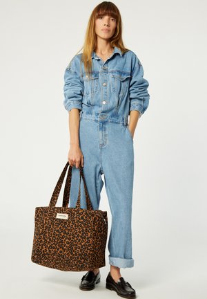 Denim jumpsuit in light blue, complemented by a brown leopard-print tote bag with sturdy straps and a label. Black loafers complete the look.