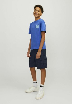 Camiseta de algodón azul con gráfico de "Frozen" en el pecho, combinada con pantalones cortos cargo de color azul marino oscuro y zapatillas blancas con detalles en negro.