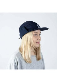 Tummansininen hattu, jossa on litteä lippa, fleece-korvaläpät ja logo edessä. Siinä on pörröinen kangas ja säädettävä leukahihna.