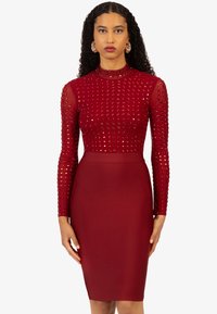 Rotes Kleid mit langen, durchsichtigen Ärmeln, die mit kleinen Nieten verziert sind, und einem taillierten Oberteil, das in einen glatten Bleistiftrock übergeht.