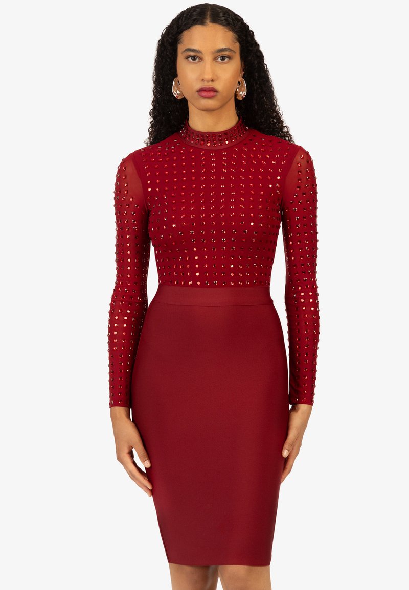 Rotes Kleid mit langen, durchsichtigen Ärmeln, die mit kleinen Nieten verziert sind, und einem taillierten Oberteil, das in einen glatten Bleistiftrock übergeht.