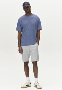 Mörkblå herrskjorta med korta ärmar i texturerad tyg, matchad med ljusgrå shorts. Tillbehör inkluderar vita strumpor och krämfärgade sneakers med svarta ränder.