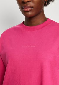 Vaaleanpunainen huppari, jossa on pyöreä kaula-aukko. Materiaali näyttää pehmeältä ja ribatulta kauluksessa. Teksti "Marc O'Polo DENIM" on hienovaraisesti esillä.