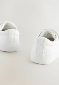 Baskets blanches en matériau synthétique lisse avec un design bas, dotées d'un collier rembourré et d'une semelle extérieure en caoutchouc texturé.